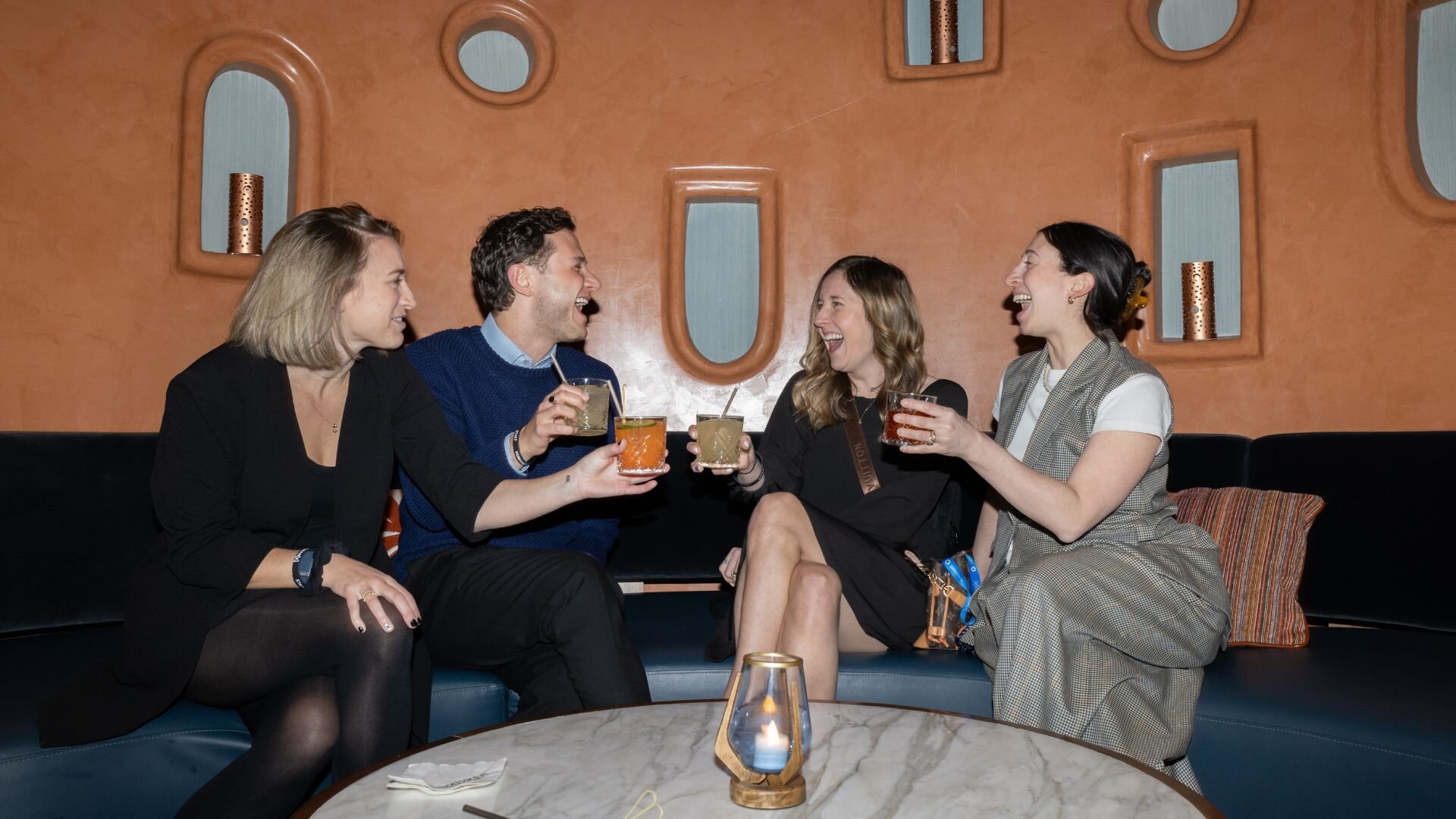 four people sitting on a couch hold their drinks up for a cheers